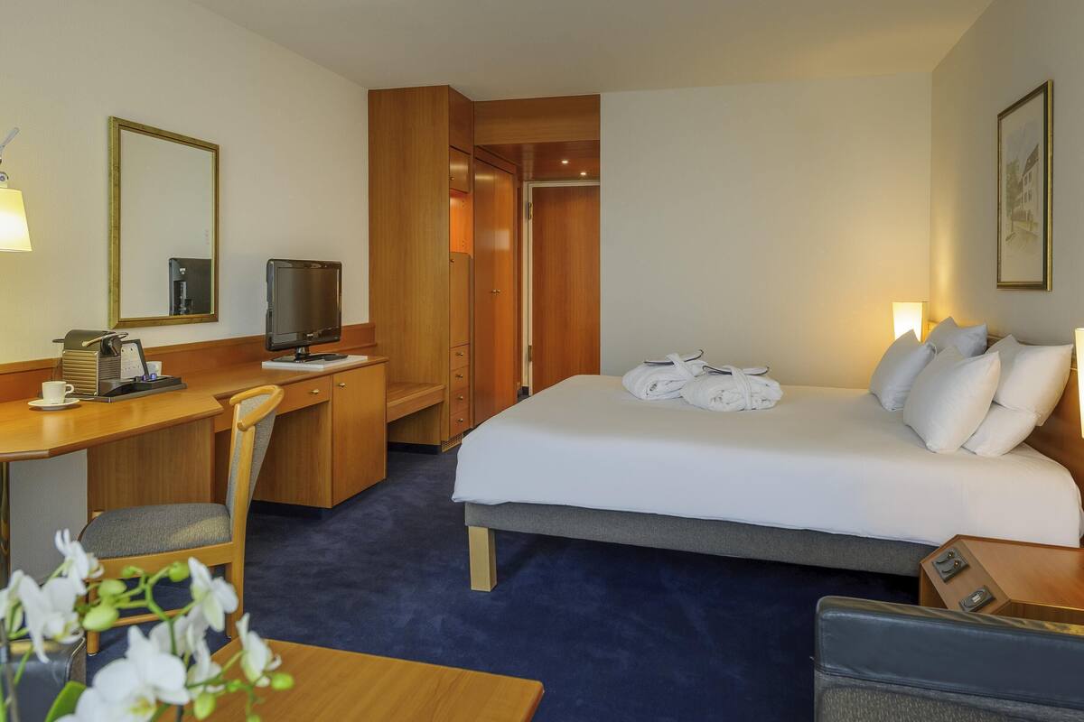 Een hotelkamer met een bed, bureau, stoel, televisie en een kleine tafel met bloemen.