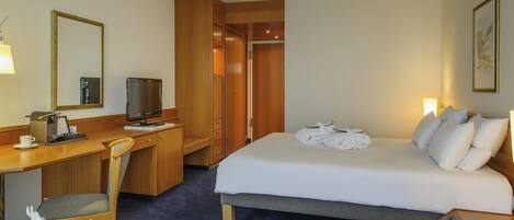 Ein Hotelzimmer mit Bett, Schreibtisch, Stuhl, Fernseher und einem kleinen Tisch mit Blumen.