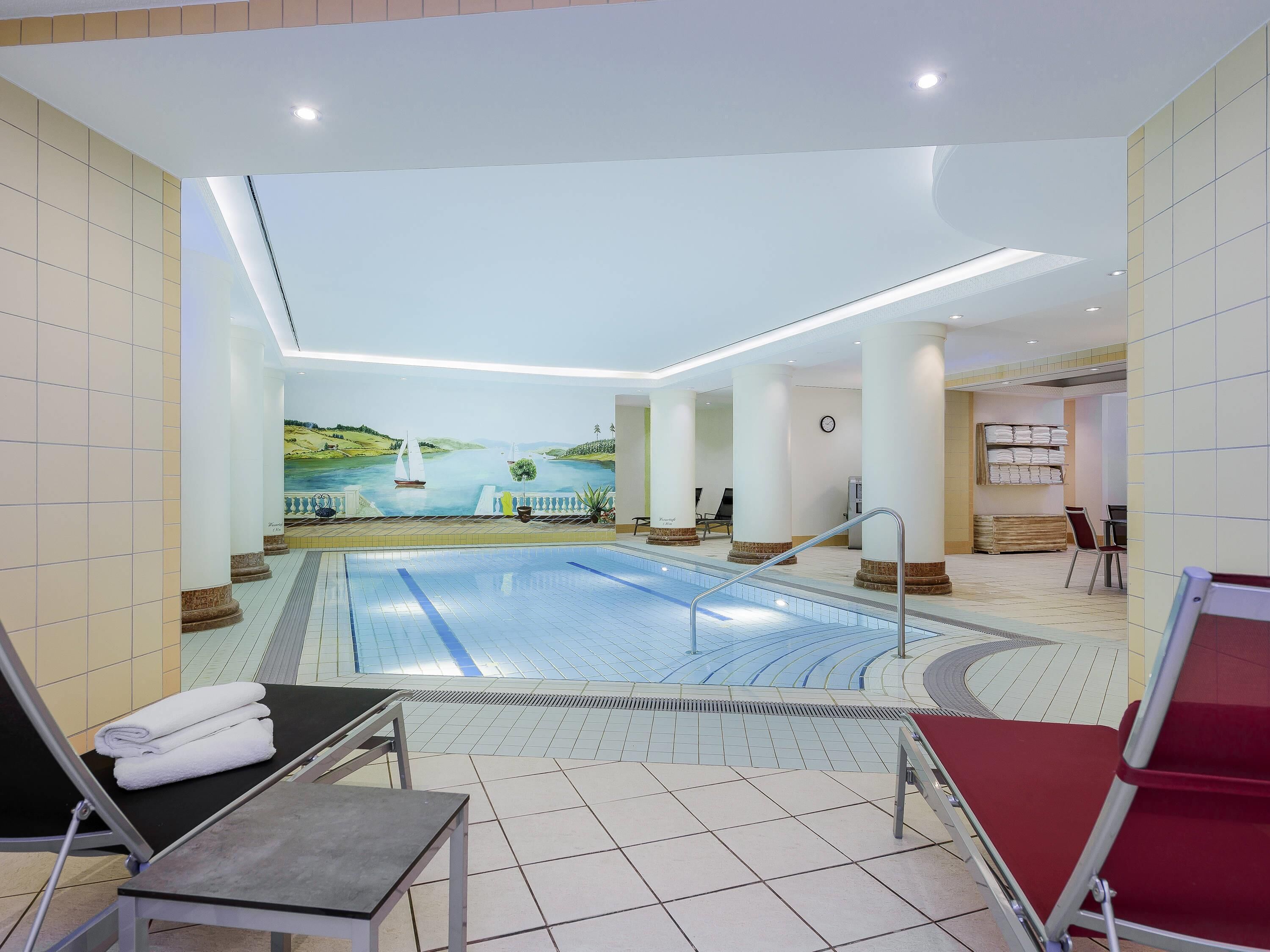 A swimming pool with a mural of a landscape and sailboats, surrounded by columns and lounge chairs.