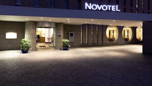 L’extérieur d’un hôtel Novotel, doté d’une architecture moderne, se caractérise par une entrée imposante, des plantes en pot et des fenêtres de forme circulaire.