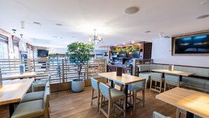 A modern restaurant with wooden tables and benches, a large TV screen, and a potted plant. - Sandman Hotel & Suites Prince George (Prince George)