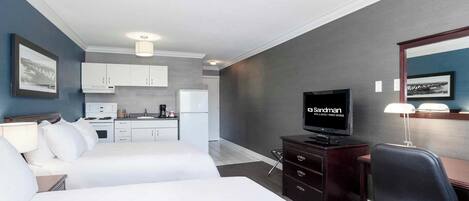 A hotel room with two beds, a desk, a television, and a kitchenette in the background.