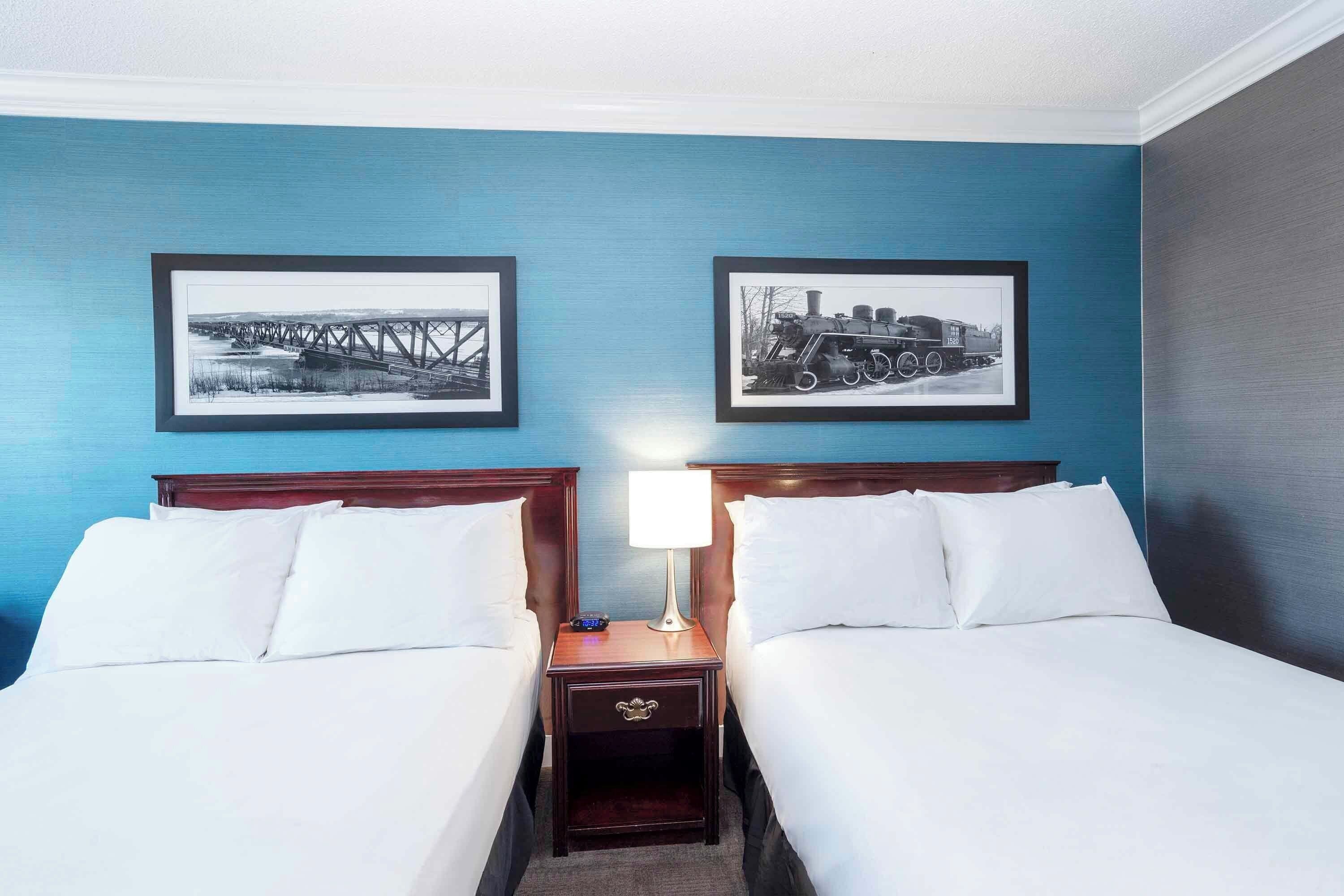 Una habitación de hotel con dos camas, una mesita de noche con lámpara y dos cuadros en la pared.