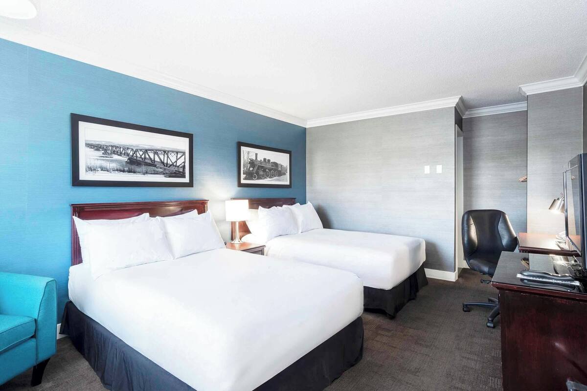 A hotel room with two beds, a desk, a chair, and two framed pictures on the wall.