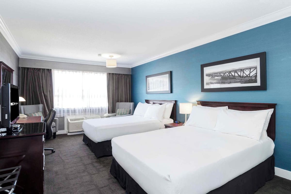 A hotel room with two beds, a desk, a chair, a TV, and a window with curtains.