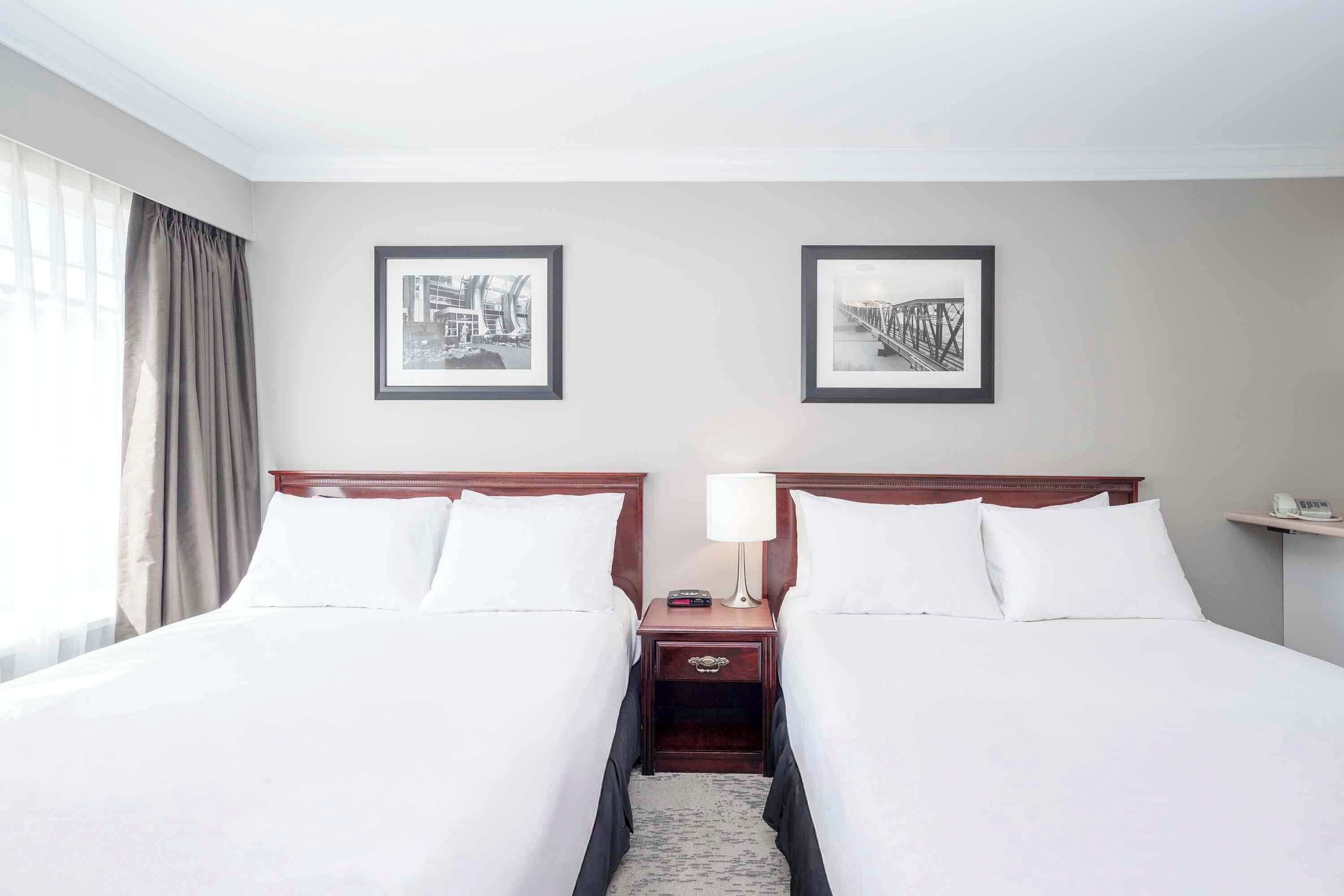 A hotel room with two beds, a nightstand with a lamp, and two framed pictures on the wall.
