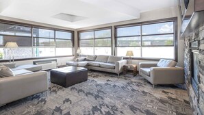 A spacious living room with large windows, a sectional sofa, a coffee table, and a fireplace. - Sandman Hotel & Suites Prince George (Prince George)