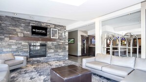 A modern lobby with a stone wall, a fireplace, and a flat-screen TV displaying 'Sandman Hotel & Suites'. - Sandman Hotel & Suites Prince George (Prince George)