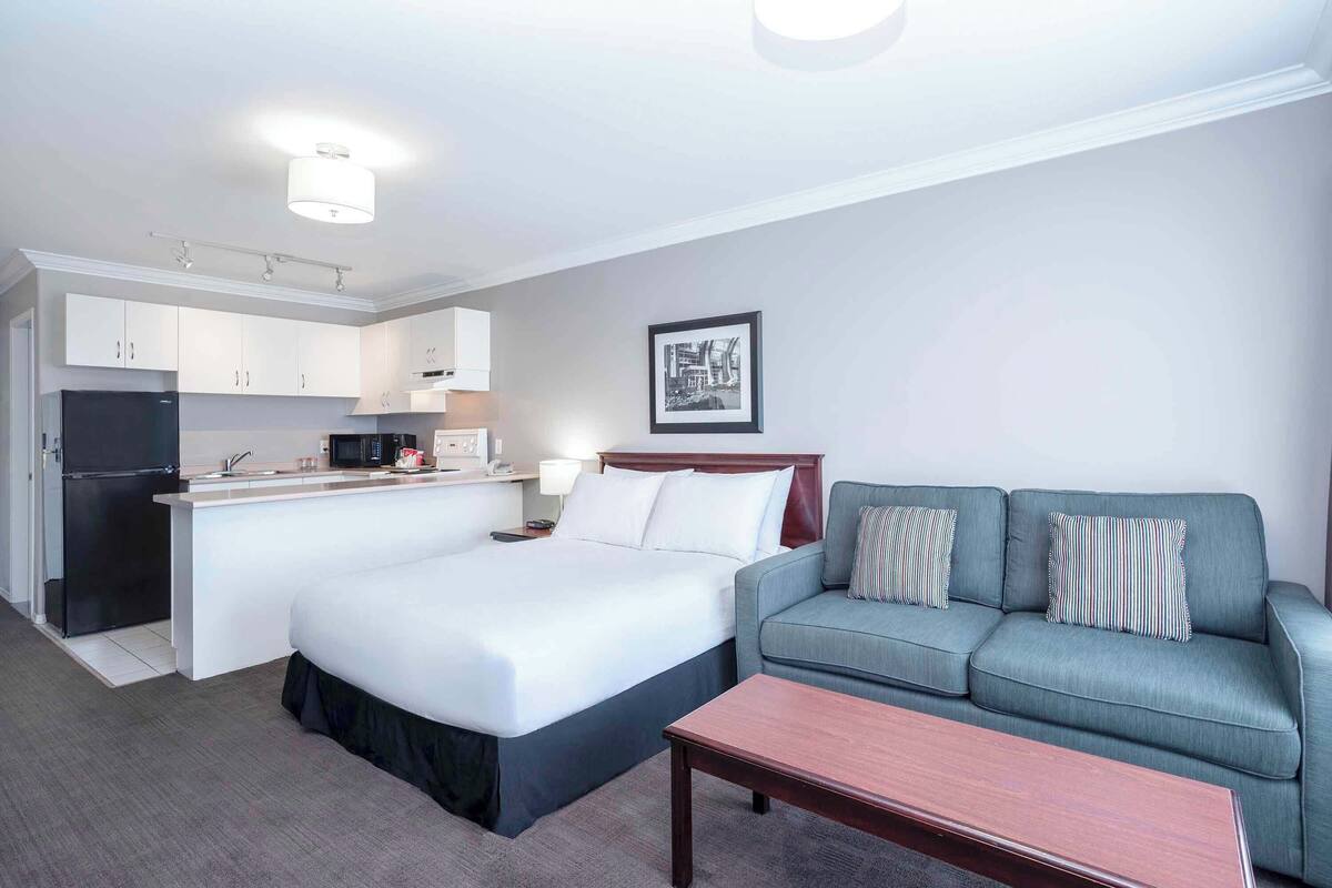 A hotel room with a bed, a sofa, a small table, a kitchenette, and a framed picture on the wall.