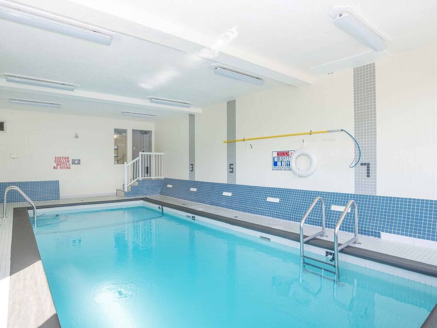 Una piscina interior con señalización clara, una estación de socorristas y suelo de baldosas.