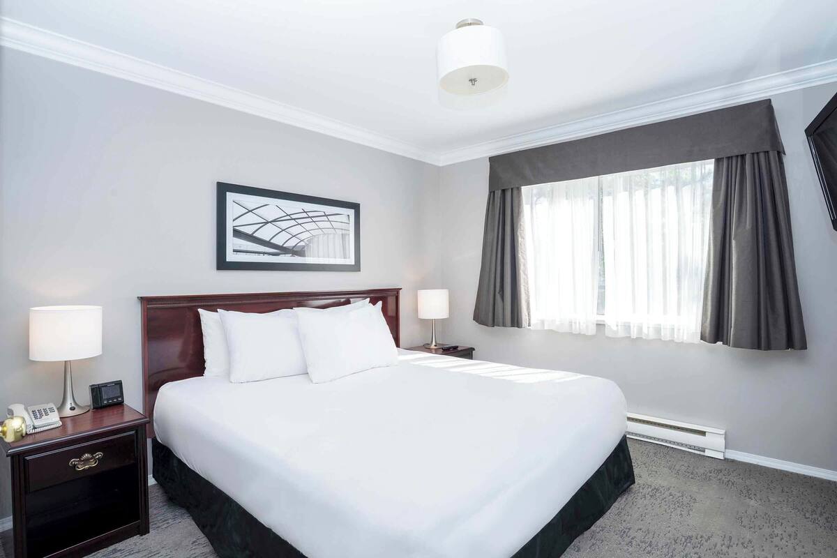 A hotel room with a large bed, two bedside tables with lamps, a framed artwork on the wall, and a window with curtains.