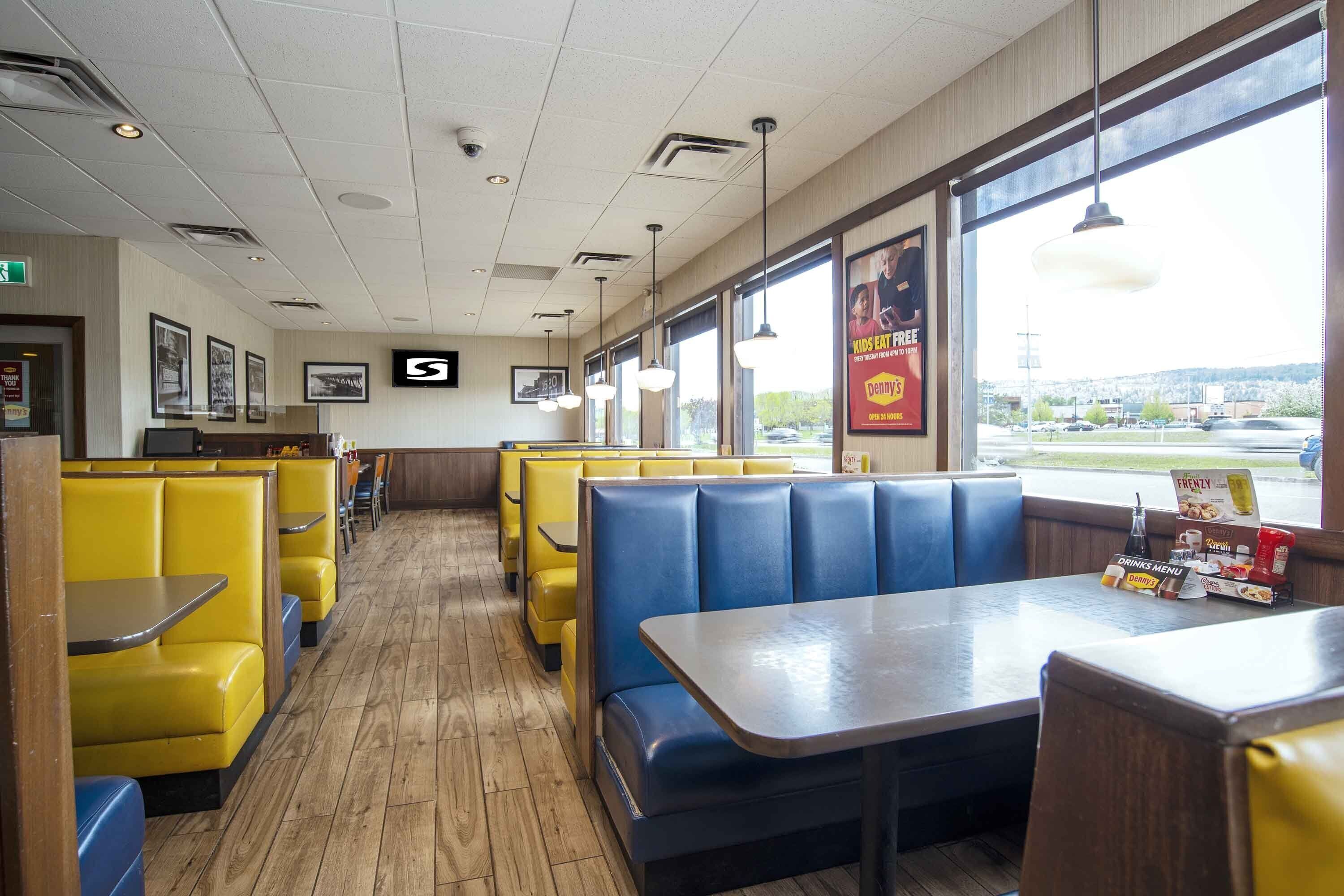 A restaurant interior with booths and tables, wooden flooring, and large windows offering a view.