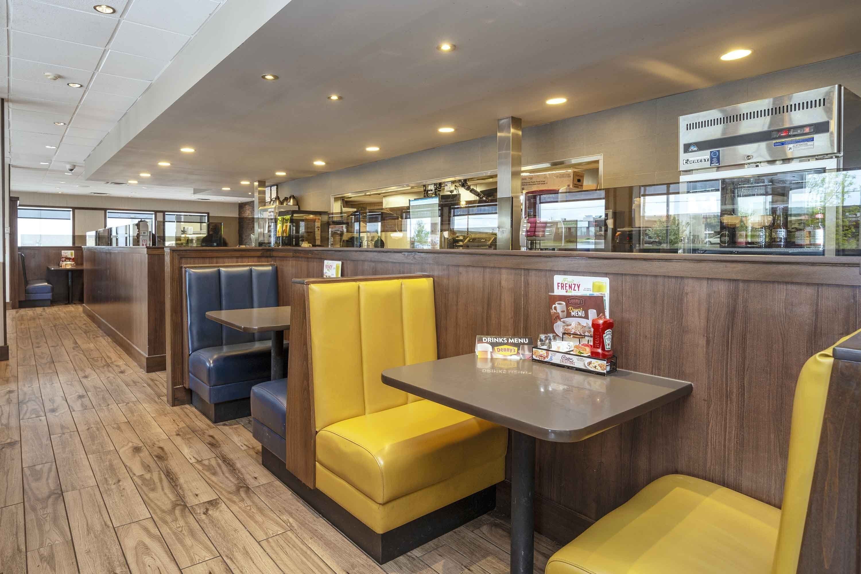 A restaurant interior with booths and tables, a drinks menu, and a counter with kitchen equipment.