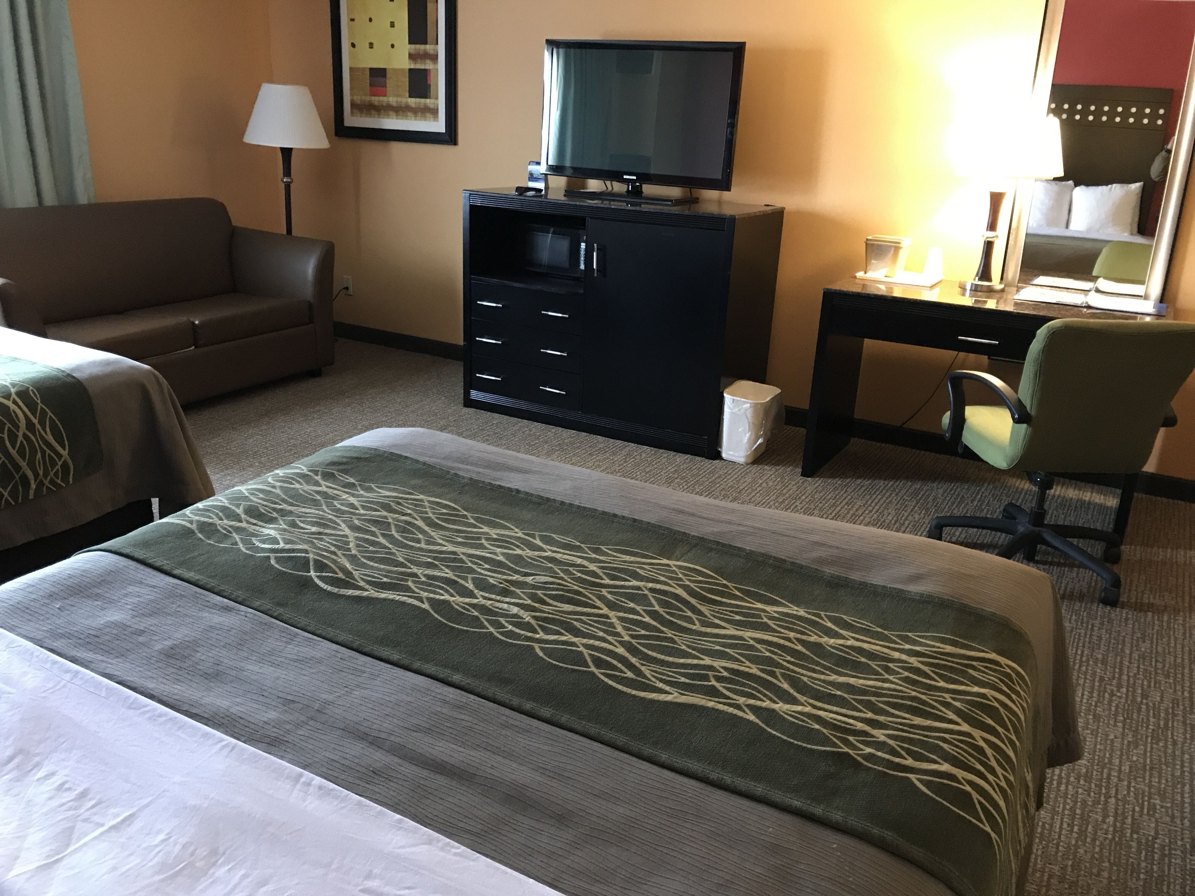 A hotel room with a bed, a desk, a chair, a television, and a lamp.