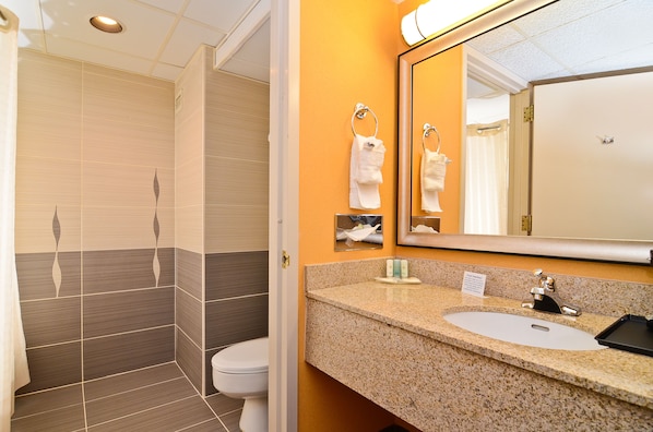 A bathroom with a shower, toilet, sink, and mirror.