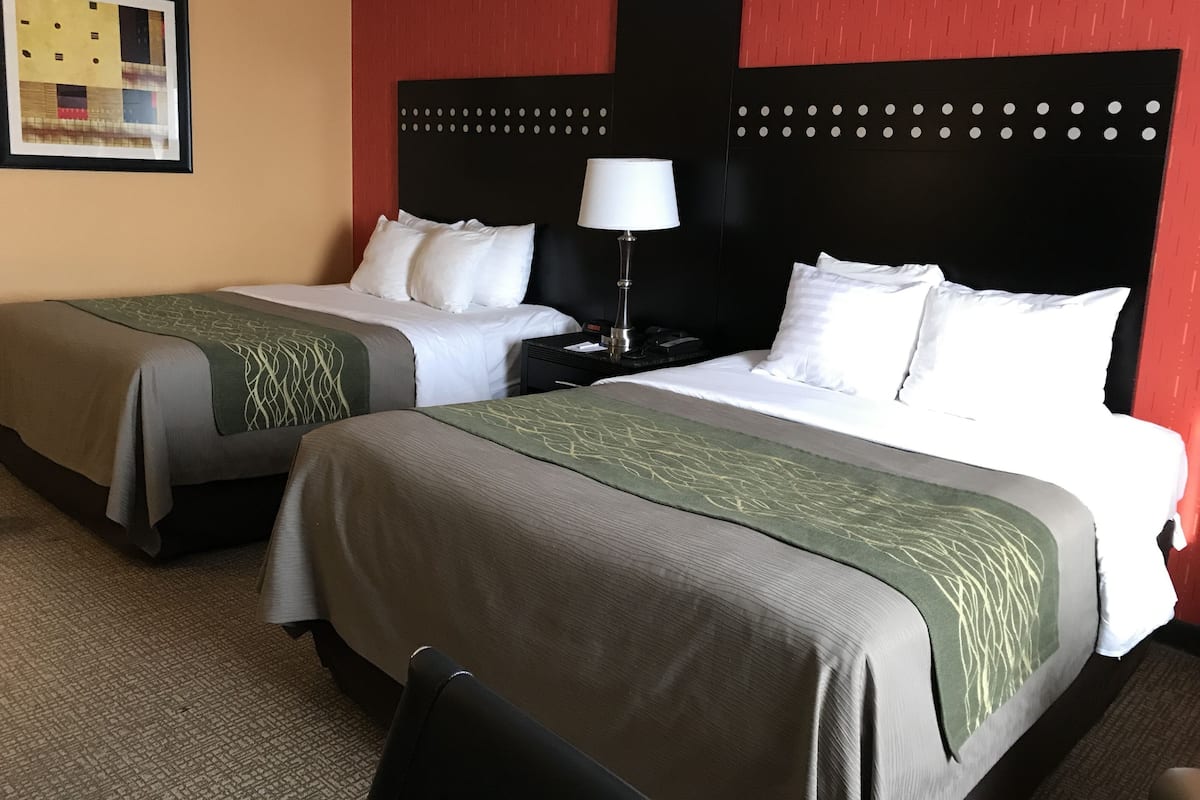 Une chambre d’hôtel avec deux lits, une table de chevet, une lampe et un tableau encadré au mur.