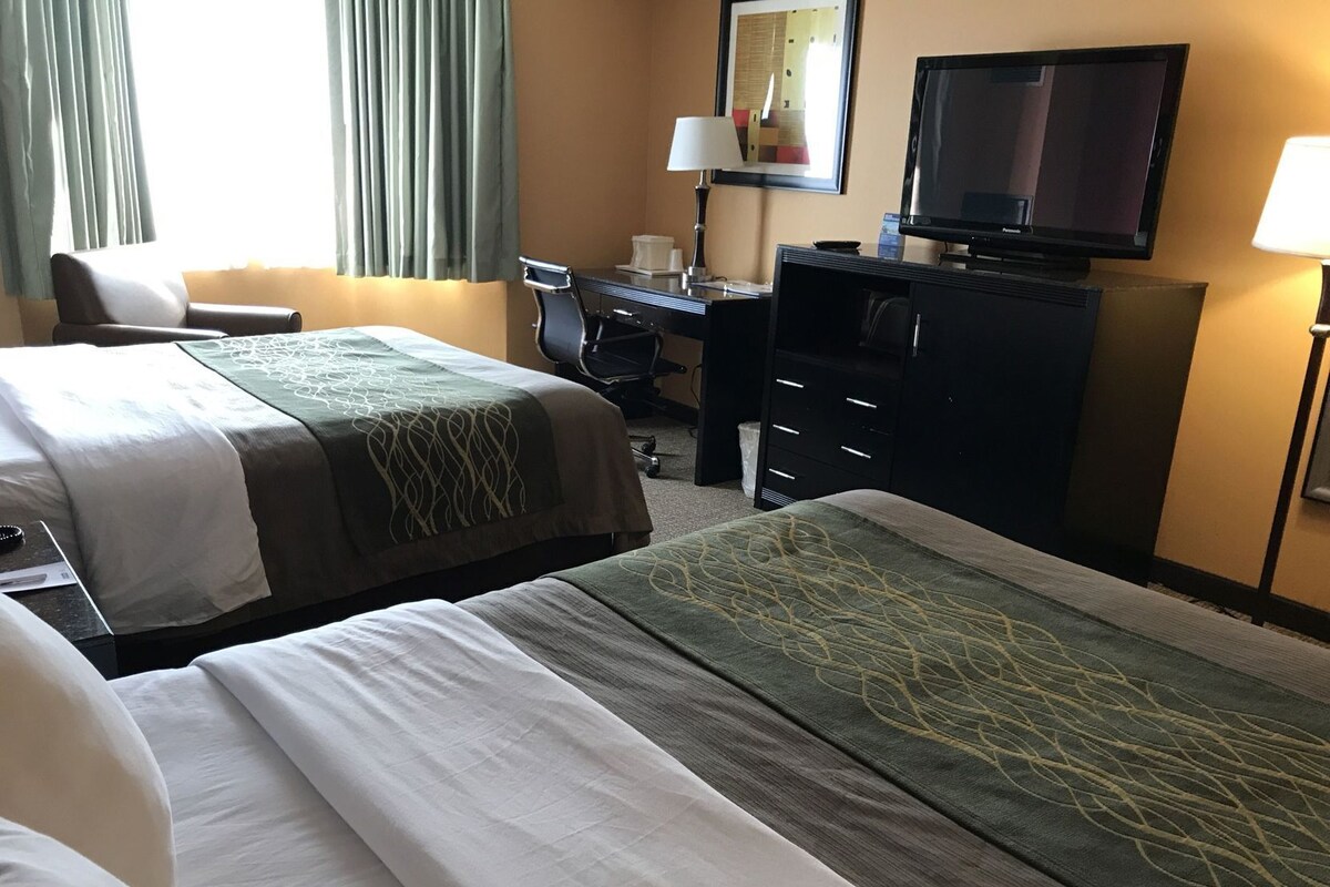 Une chambre d’hôtel avec deux lits, un bureau, une chaise, une télévision et une lampe.