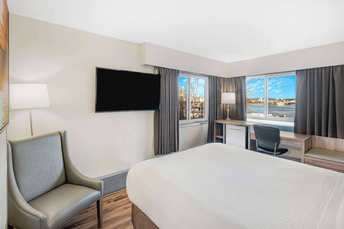 A hotel room with a large bed, a desk, a chair, a TV, and a view of the city.