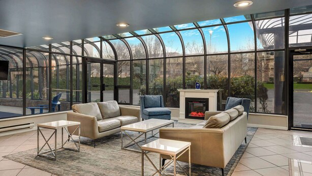A spacious living area with a glass enclosure, leather sofas, and a fireplace. - Days Inn by Wyndham Victoria On The Harbour (Victoria)