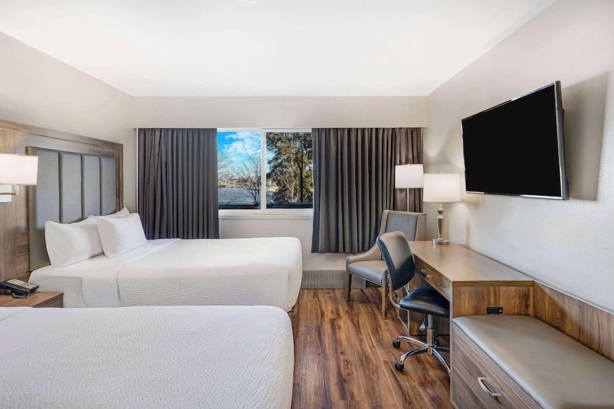Une chambre d’hôtel avec deux lits, un bureau, une chaise, une télévision et une fenêtre avec des rideaux.