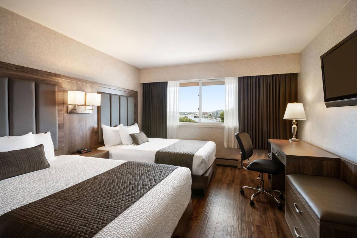 A hotel room with two beds, a desk, a chair, a TV, and a window with a city view.