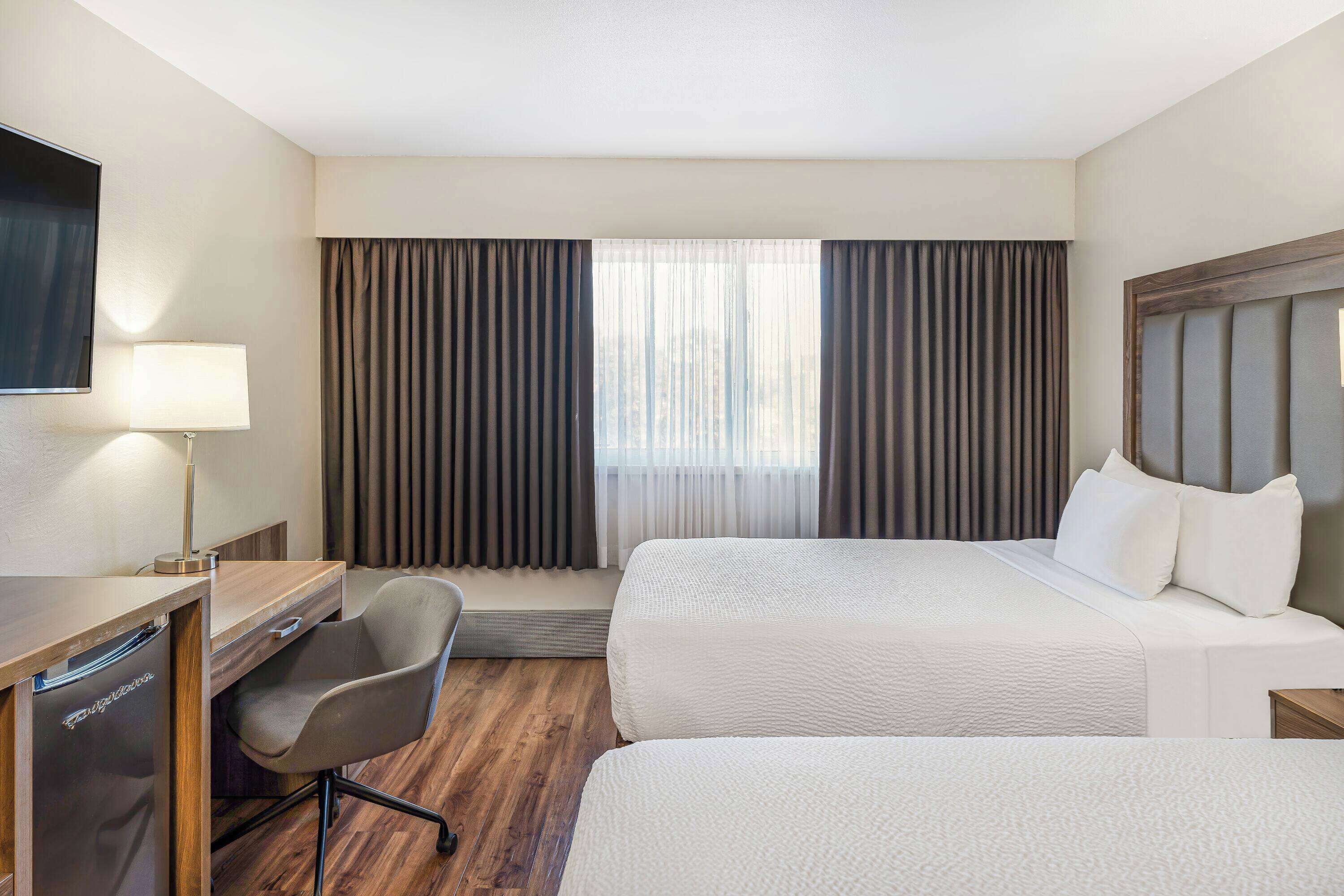 A hotel room with two beds, a desk, a chair, a television, and a window with curtains.