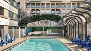 A swimming pool with blue chairs and a covered seating area, surrounded by a fence and a building with balconies. - Days Inn by Wyndham Victoria On The Harbour (Victoria)