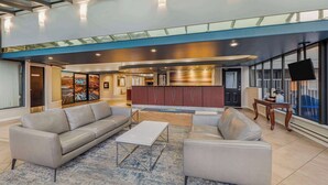 A spacious lobby with a modern design, featuring a sofa, armchair, and coffee table. A kitchen area is visible in the background, and there is a large window providing a view of the outdoors. - Days Inn by Wyndham Victoria On The Harbour (Victoria)