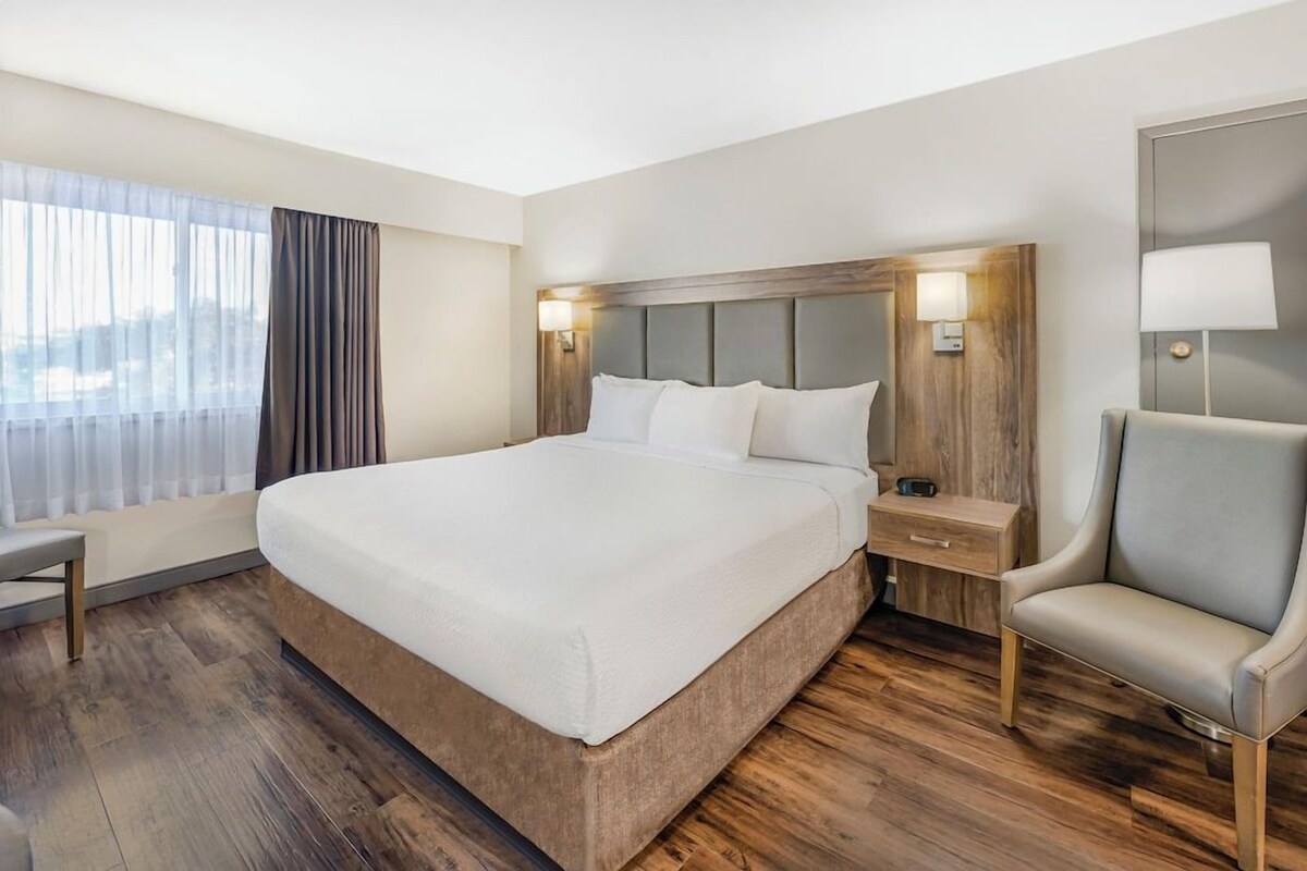 A hotel room with a large bed, bedside tables, a chair, and a window with curtains.