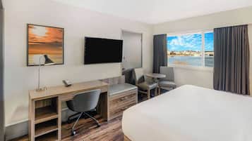 A hotel room with a bed, desk, chair, TV, and a view of the city through the window.