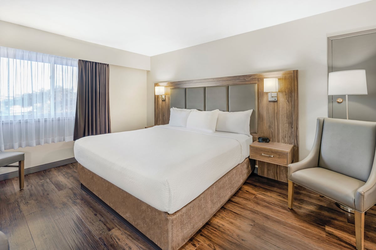 A hotel room with a large bed, bedside tables, a chair, and a window with curtains.