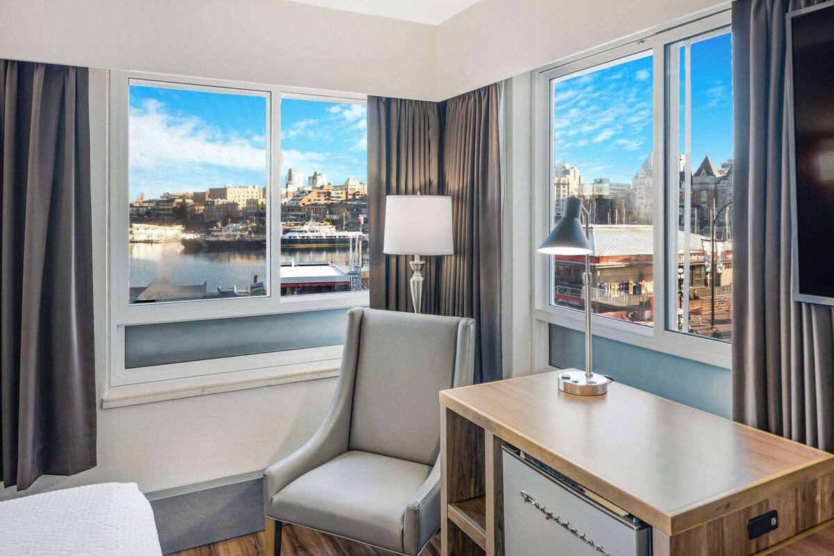 A hotel room with a city view, a desk, a chair, and a TV.