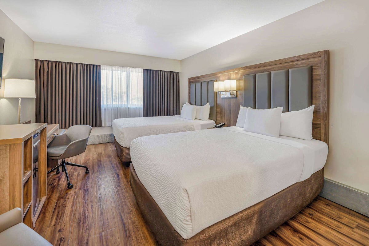 A hotel room with two beds, a desk, a chair, and a large window with curtains.