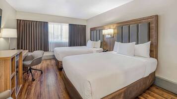 A hotel room with two beds, a desk, a chair, and a large window with curtains.