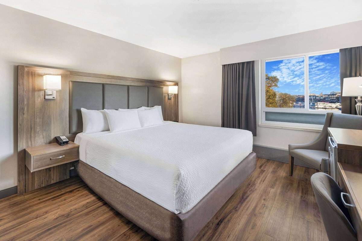 A hotel room with a large bed, bedside tables, a desk, and a window with a city view.