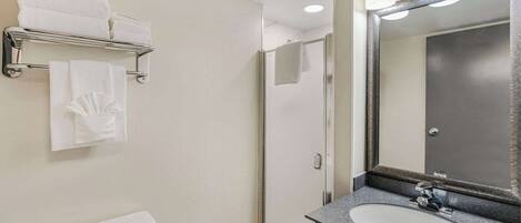A bathroom with a white toilet, a sink with a large mirror, and a towel rack with folded towels.