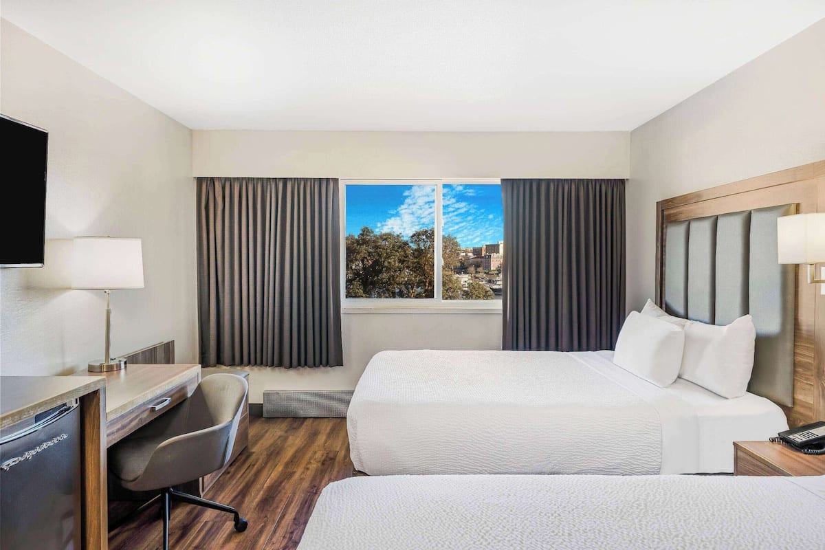 A hotel room with two beds, a desk, a chair, a TV, and a window with curtains.
