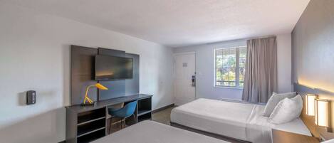 Une chambre d’hôtel avec deux lits, un bureau, une télévision et une fenêtre avec des rideaux.
