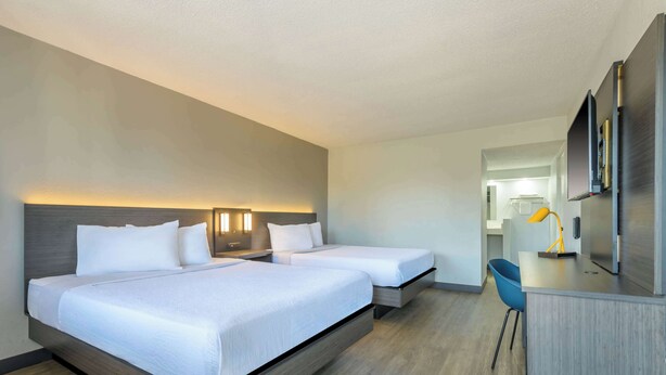 A hotel room with two beds, a desk, a chair, and a mirror.