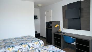 Une chambre d’hôtel de taille réduite, comprenant un lit, un bureau, une chaise, une télévision et une petite kitchenette.