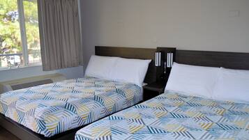 A hotel room with two beds, each with a patterned bedspread, a bedside table with a lamp, and a window with curtains.