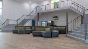 A spacious lobby with a modern staircase, seating area, and vending machine.