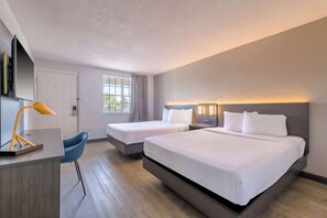 A hotel room with a large bed, two smaller beds, a desk, a chair, and a TV.