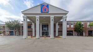 A motel with a prominent '6' sign, a covered entrance with columns, and a brick building in the background.