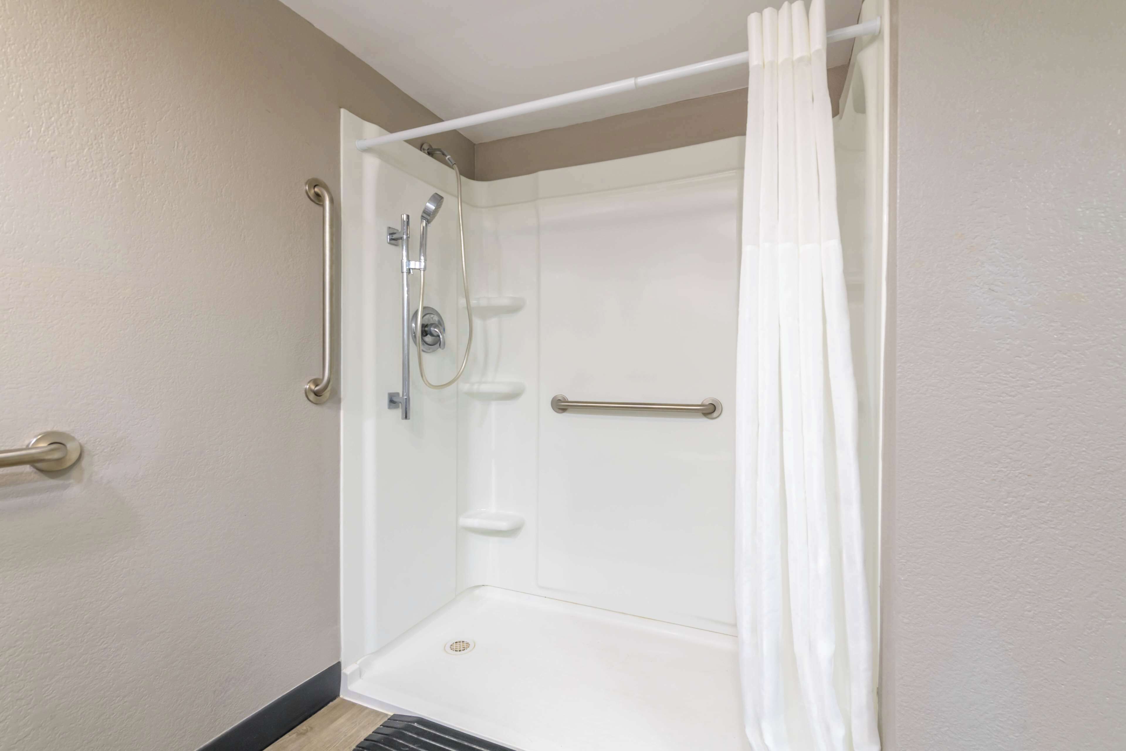 A corner shower with a white curtain, a grab bar, and a handheld showerhead.