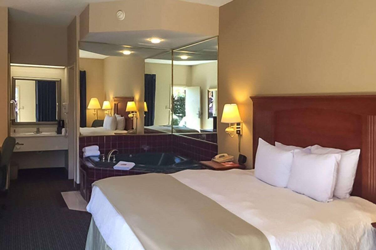 Ein Hotelzimmer mit einem großen Bett, einem separaten Badezimmer mit Badewanne, einem Schreibtisch und einem Spiegel.