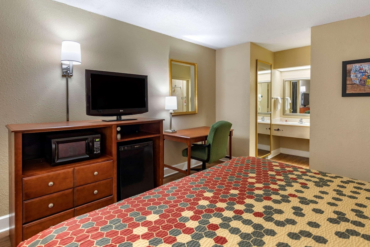 Una habitación de hotel con cama, escritorio, televisor, microondas, silla y espejo.