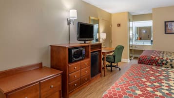 A hotel room with a bed, a desk with a television, a chair, a microwave, and a dresser.