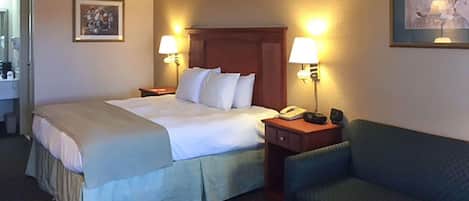 A hotel room with a bed, two bedside tables, a chair, a small table, and a painting on the wall.