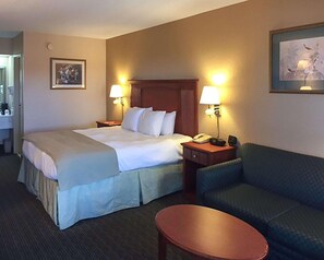 A hotel room with a bed, two bedside tables, a chair, a small table, and a painting on the wall. - Econo Lodge Cordele (Cordele)